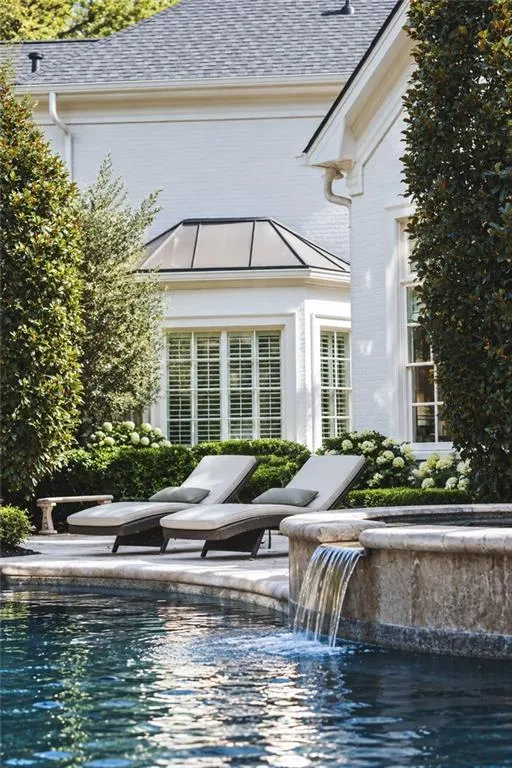 Swimming pool with integrated waterfall feature, stone coping, and surrounding mature landscaping