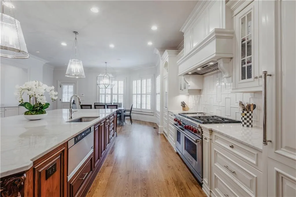 Gourmet kitchen featuring a large central island with integrated sink, stainless steel appliances, custom white cabinetry, and hardwood flooring