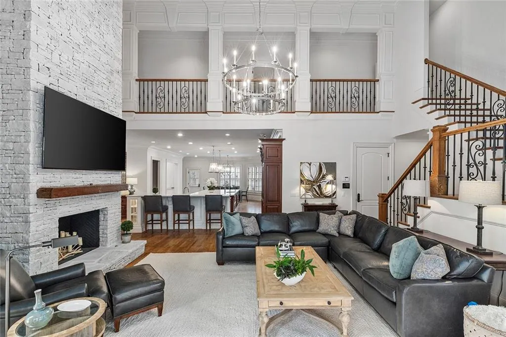Living area with a chandelier, wood finished floors, crown molding, a stone fireplace, and a high ceiling