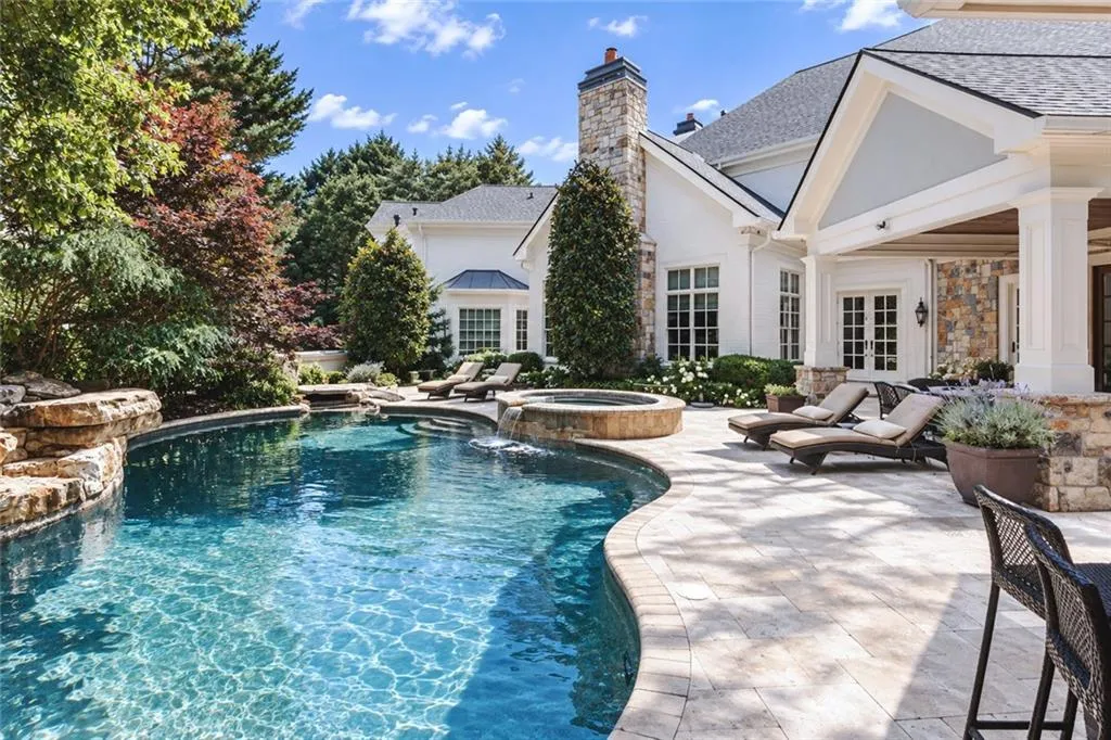 Curved swimming pool with an integrated spa, surrounded by a stone patio and lush landscaping