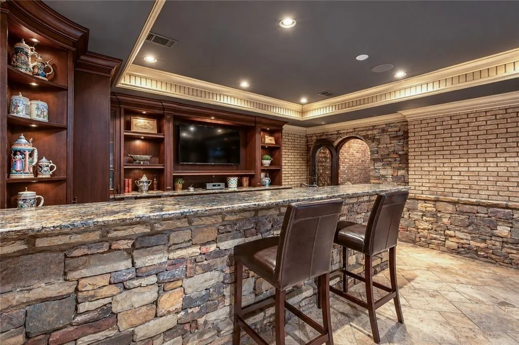 Stone-clad bar with a granite countertop, built-in wooden shelving, integrated television, recessed lighting, and crown molding