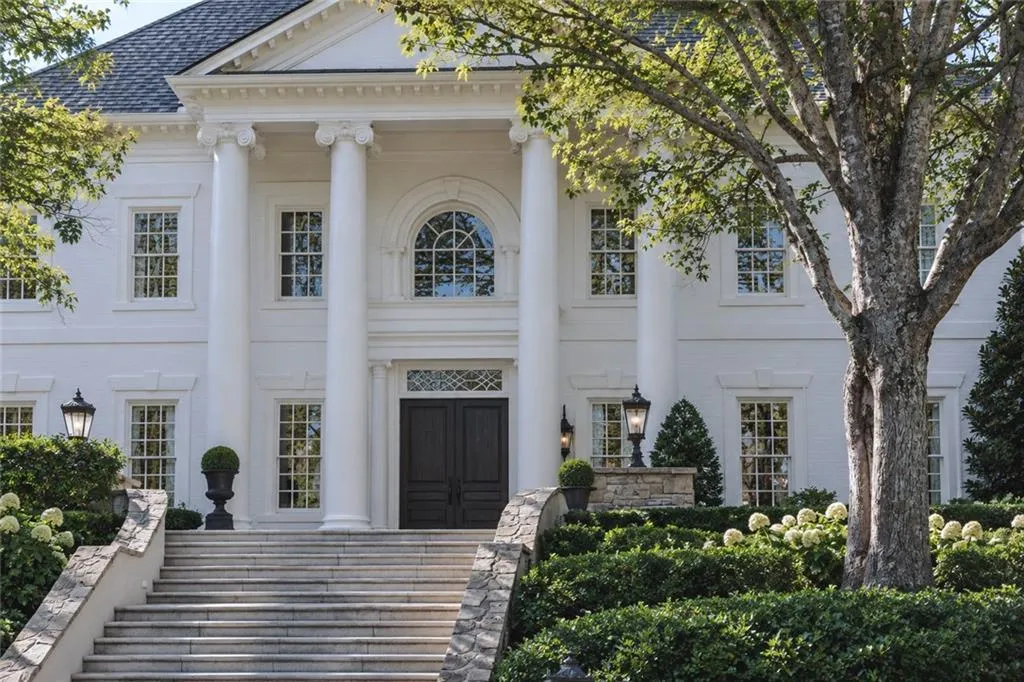 White painted brick exterior with a columned portico, symmetrical windows, a prominent arched window, and a grand stone staircase