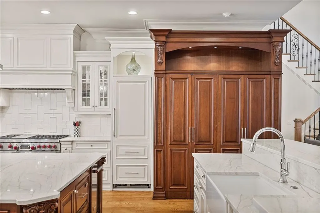 Kitchen featuring dual tone cabinets, light stone counters, light wood-style flooring, glass insert cabinets, and tasteful backsplash