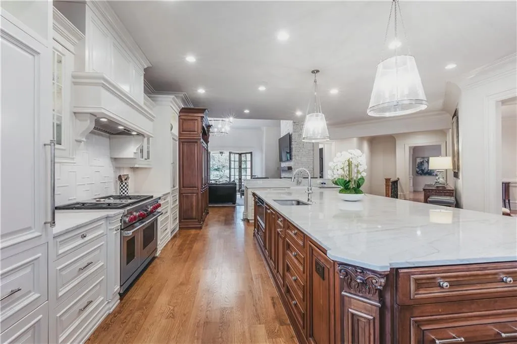Gourmet kitchen with wood-finish flooring, white cabinetry, a large center island with a light-toned countertop, and stainless steel appliances