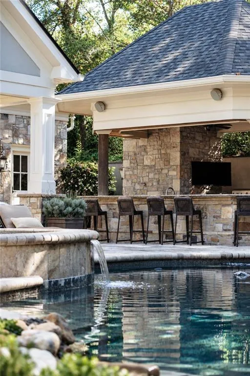 Outdoor kitchen with stone detailing and seating, featuring a built-in entertainment screen