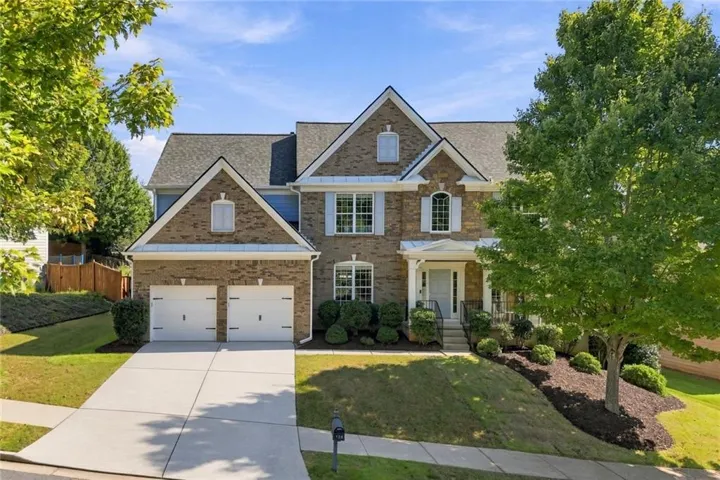 Brick facade with white shutters, two-car garage, covered entry porch, and a sloped, landscaped front yard