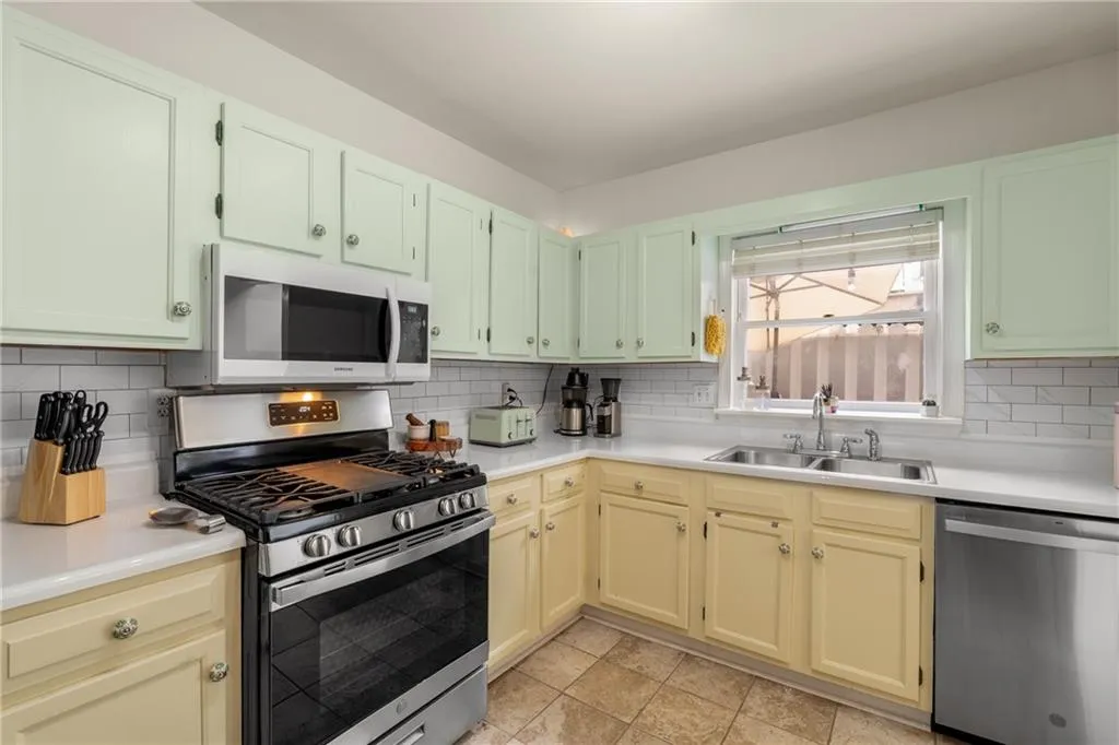 Kitchen featuring light tile patterned floors, stainless steel appliances, backsplash, and sink