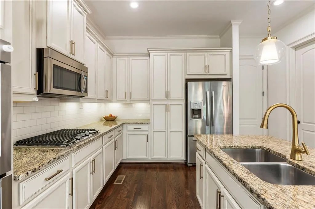 Kitchen with appliances with stainless steel finishes, dark wood-style floors, ornamental molding, decorative backsplash, and white cabinets