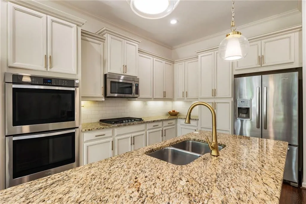 Kitchen with appliances with stainless steel finishes, ornamental molding, tasteful backsplash, light stone counters, and decorative light fixtures