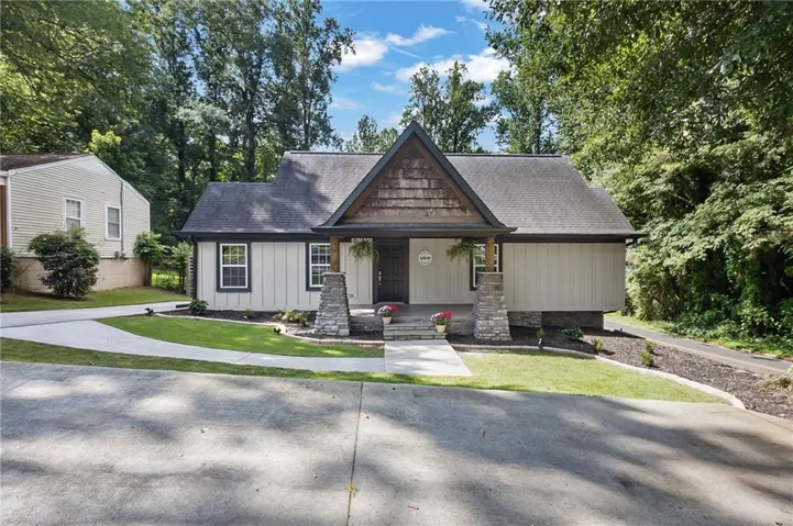 Charming cottage-style home featuring a peaked gable roof, stone foundation pillars, and light-colored exterior siding