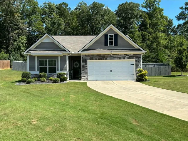 Exterior featuring a grey siding and stone facade, an attached garage with a white door, a paved driveway, and a well-maintained lawn with shrubbery