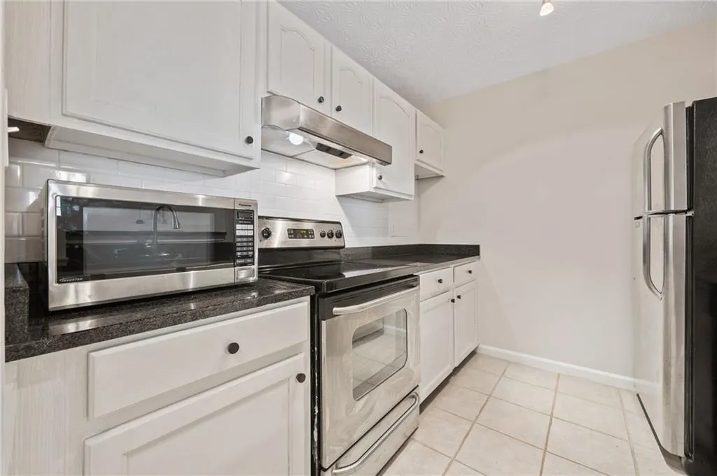Kitchen featuring under cabinet range hood, tasteful backsplash, baseboards, white cabinets, and appliances with stainless steel finishes