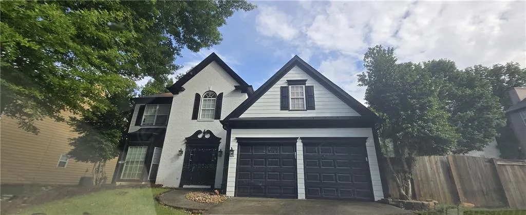 Two-story stucco and siding exterior featuring gabled rooflines, a two-car garage with black doors, decorative arched windows, and a covered entry