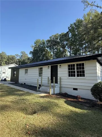 White horizontal siding exterior with a black metal roof, featuring a dark entry door, multiple pane windows, and exterior light fixtures