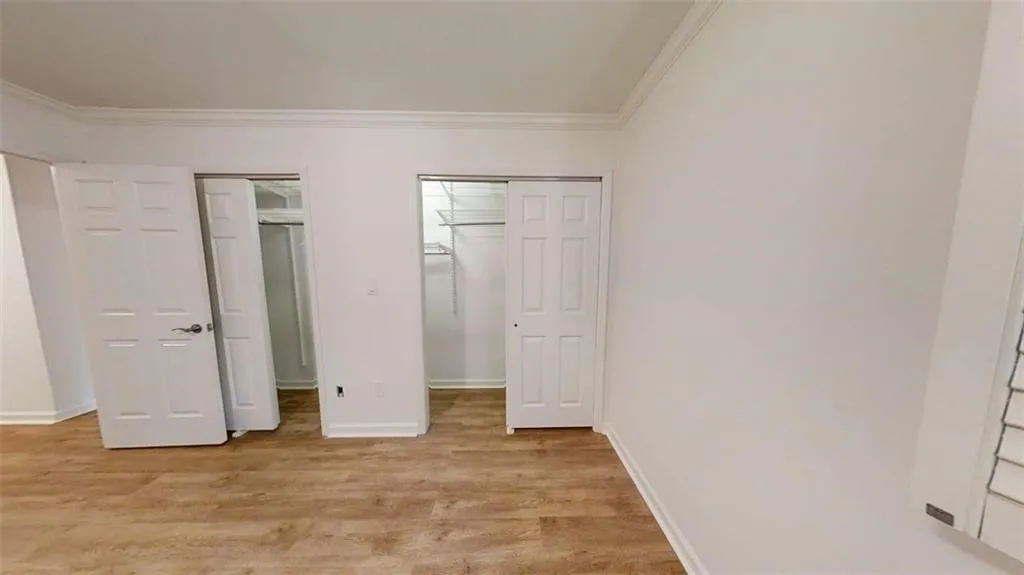 Unfurnished bedroom featuring light wood-style floors, crown molding, and two closets