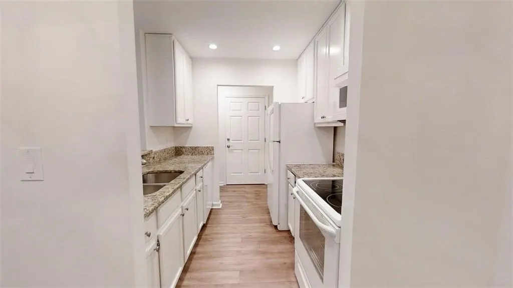 Kitchen with white appliances, white cabinetry, light stone countertops, light wood-type flooring, and recessed lighting