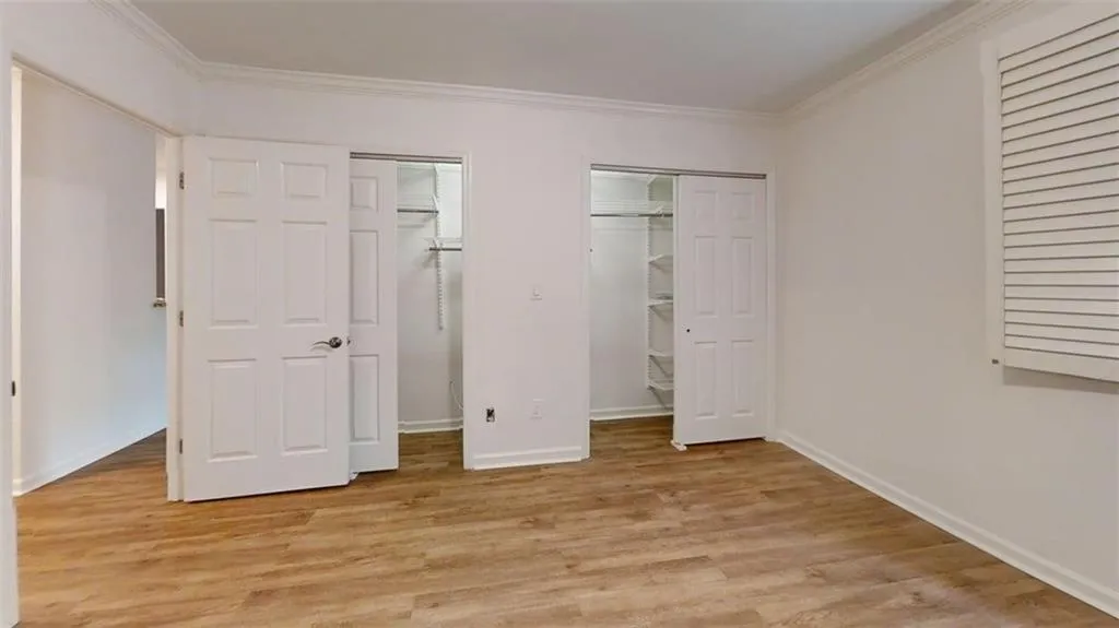 Unfurnished bedroom with multiple closets, crown molding, and light wood-type flooring