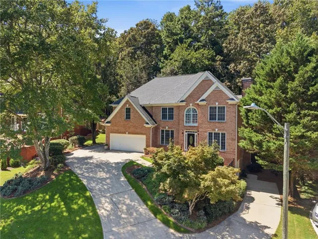 Brick exterior residence with a dual-car garage, mature landscaping, and a paved driveway
