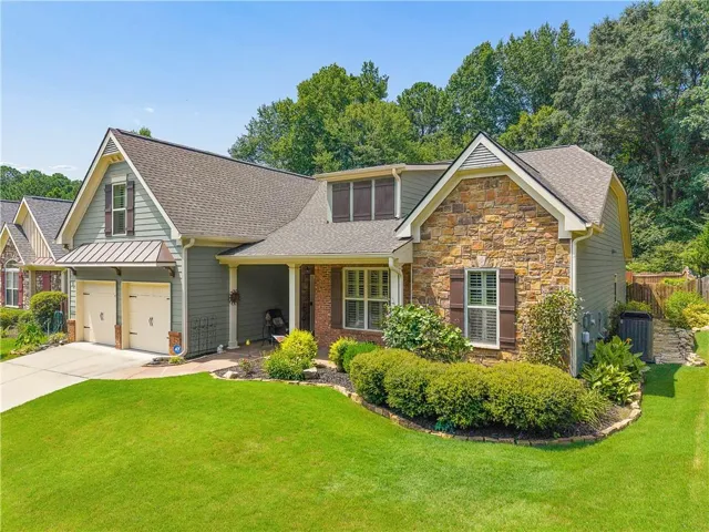 Exterior showcasing a two-car garage, stone and siding facade, covered entry, and mature landscaping