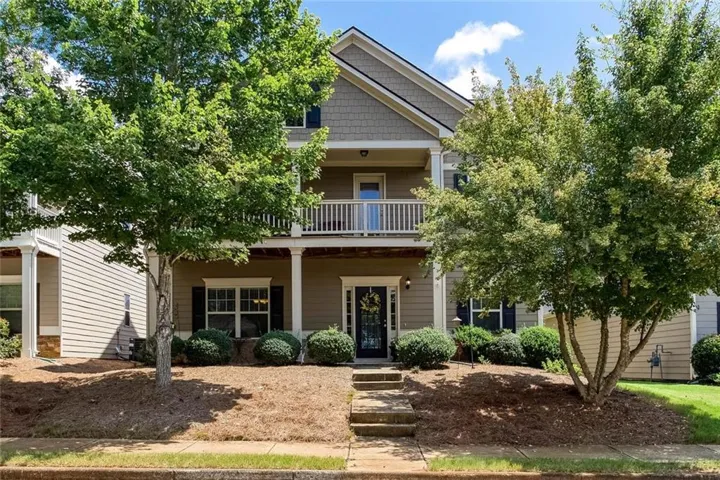 Multi-level property exterior with a second-story balcony, covered porch, and mature trees