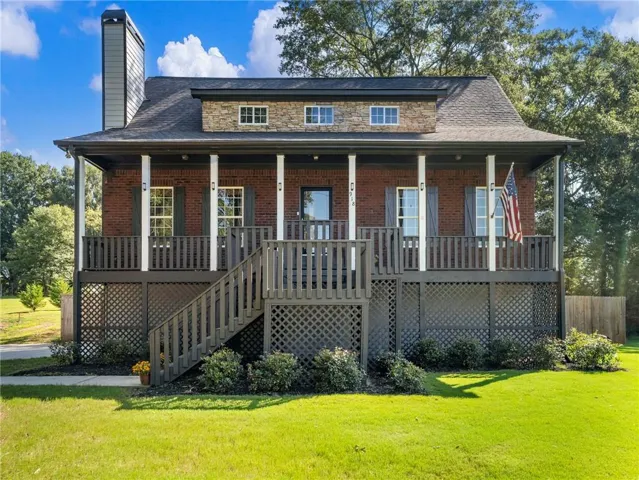 Brick exterior featuring a stone dormer, covered front porch with white columns, dark gray railing, and a matching exterior staircase