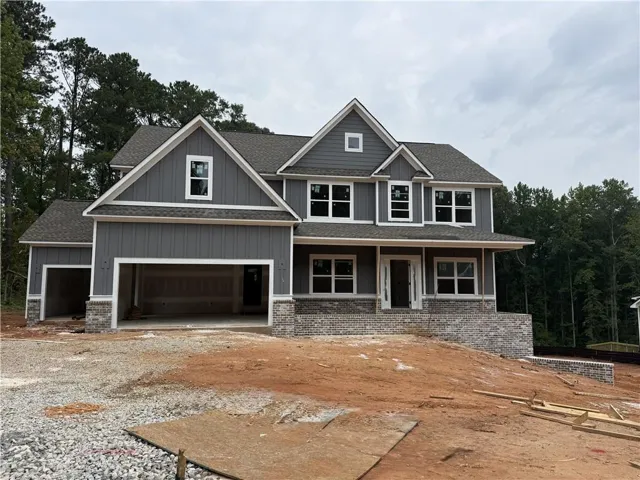 Gable roofline with gray shingles, gray board and batten siding, white window trim, and a partial stone facade