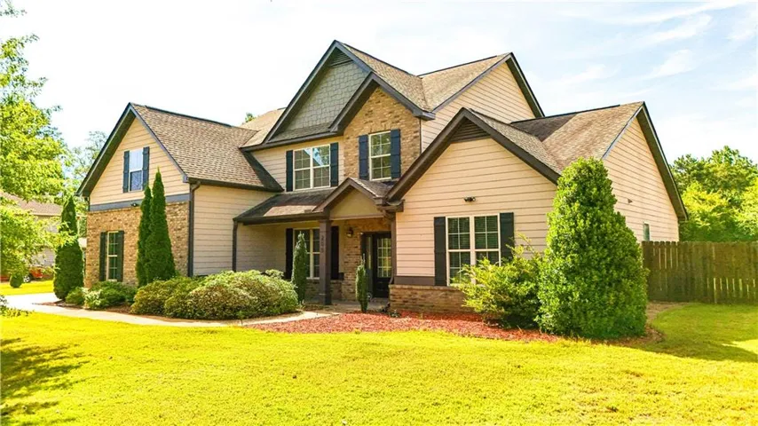 Multi-gabled roofline with dark shingles, stone and siding exterior, front porch entry, black louvered shutters, and established perimeter landscaping