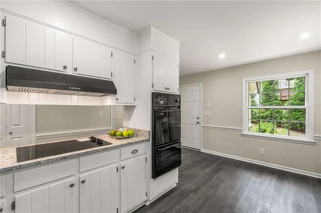 Kitchen featuring under cabinet range hood, black appliances, white cabinetry, dark wood-type flooring, and light stone countertops