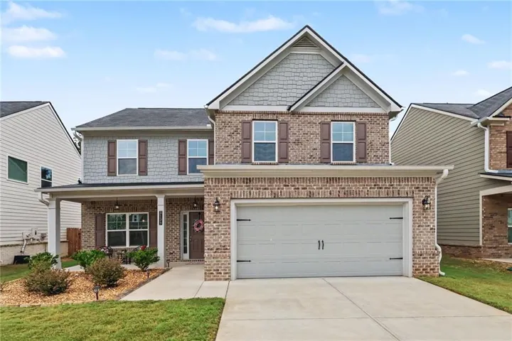 Two-story residence featuring brick and shingle siding, an attached two-car garage, covered front porch, and a concrete driveway