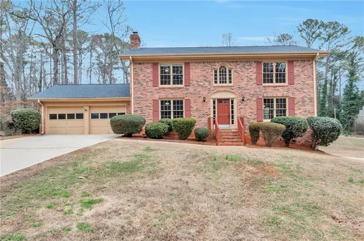 Brick exterior with red shutters, two-car garage, front entry with transom window, and mature landscaping