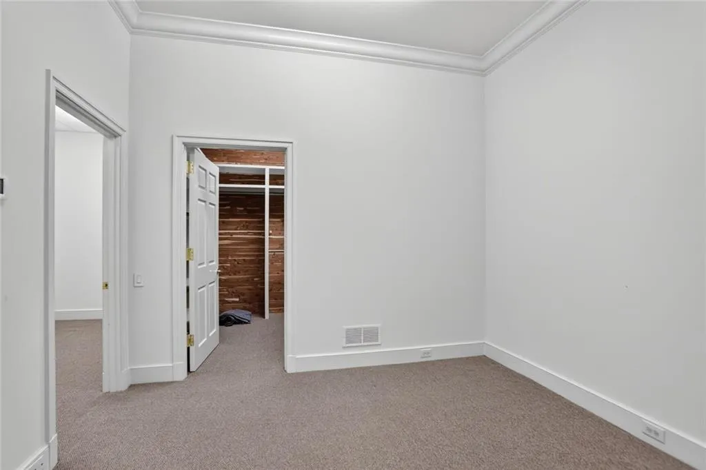 Spare room off on garage level with light carpet and crown molding.  Featuring a storage room and a cedar closet.