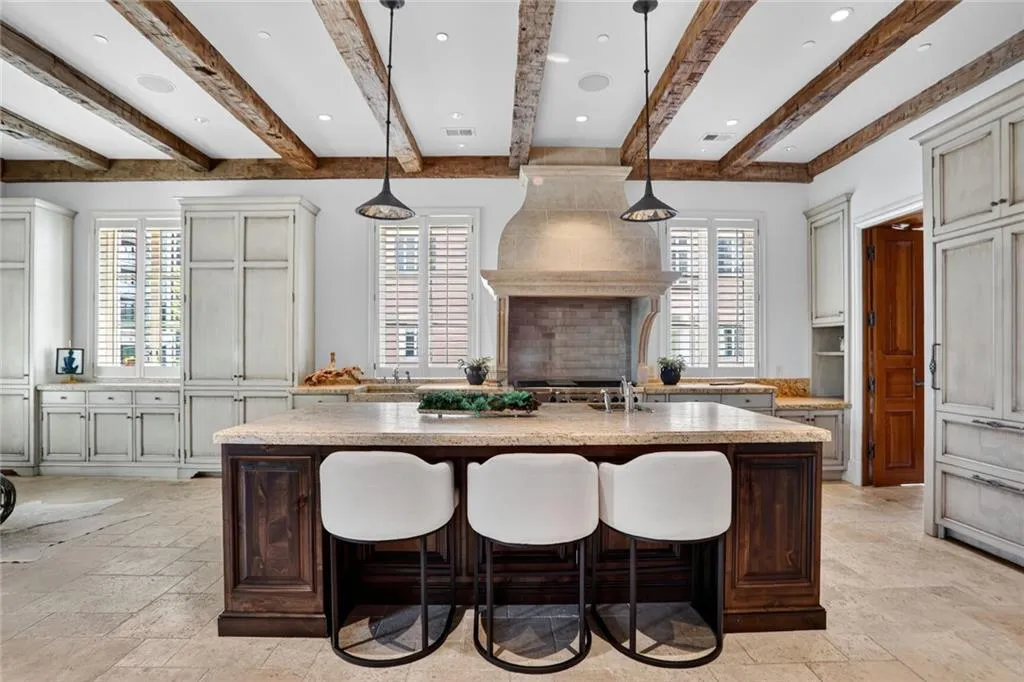 Kitchen featuring dark brown cabinets, a breakfast bar, a kitchen island with sink, stone tile flooring, and beamed ceiling