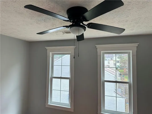 Room featuring a ceiling fan with integrated lighting, two double-hung windows with decorative trim, and light gray wall finishes