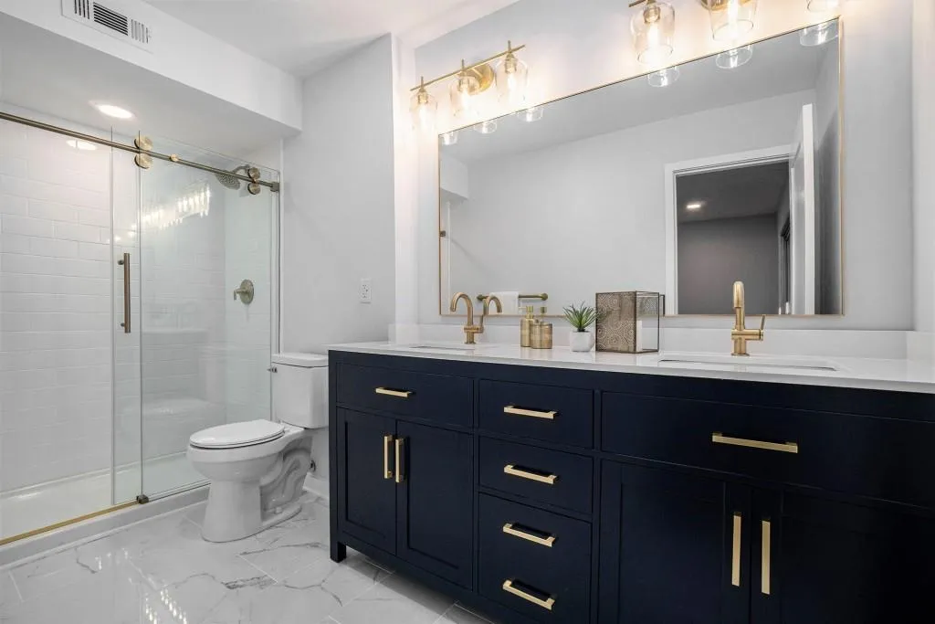 The Primary Suite boasts a Spa-Like Bathroom with a Double Stone Vanity, Marble Flooring, and a Frameless Glass Shower accented in Brass.