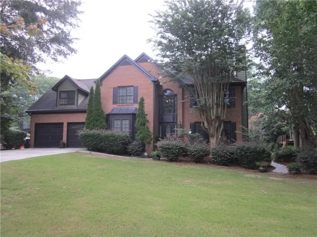 Brick exterior home with a two-car garage, dormer window, and mature landscaping