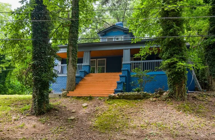 View of front of home featuring stairway, a porch, brick siding, and a chimney