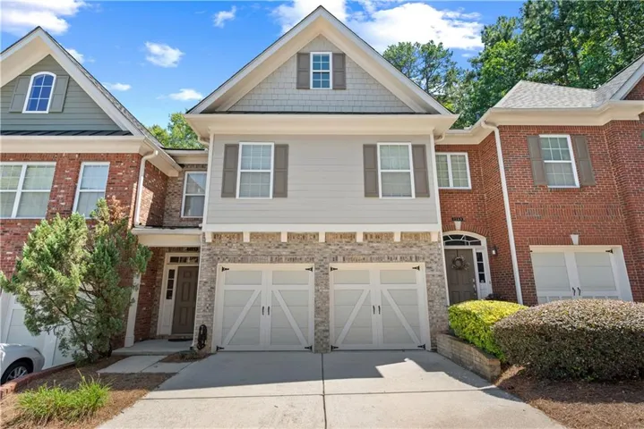 Two-car garage with carriage-style doors, brick and siding exterior, arched entry, and mature landscaping