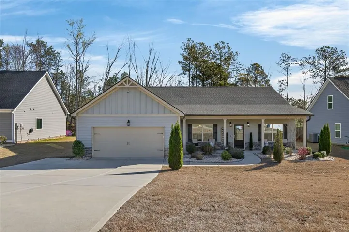 View of front facade featuring covered porch, roof with shingles, board and batten siding, concrete driveway, and an attached garage