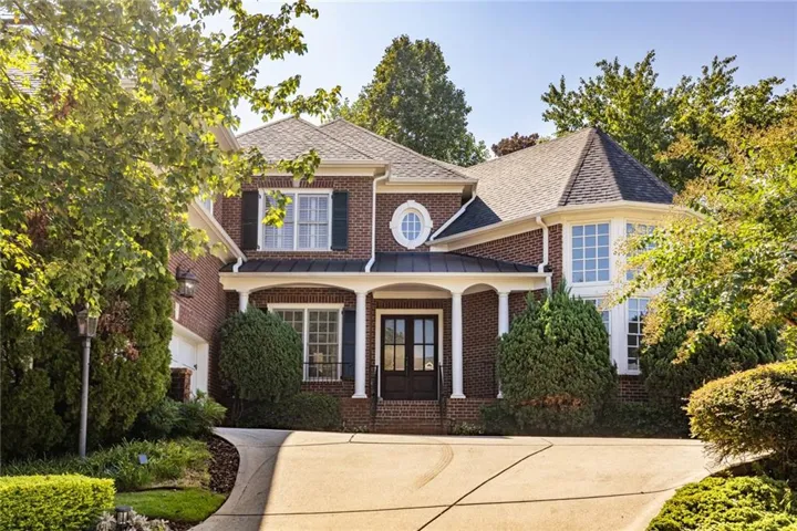 Brick exterior with white trim, covered front porch with columns, dark double entry doors, bay window with multiple panes, and a circular window feature