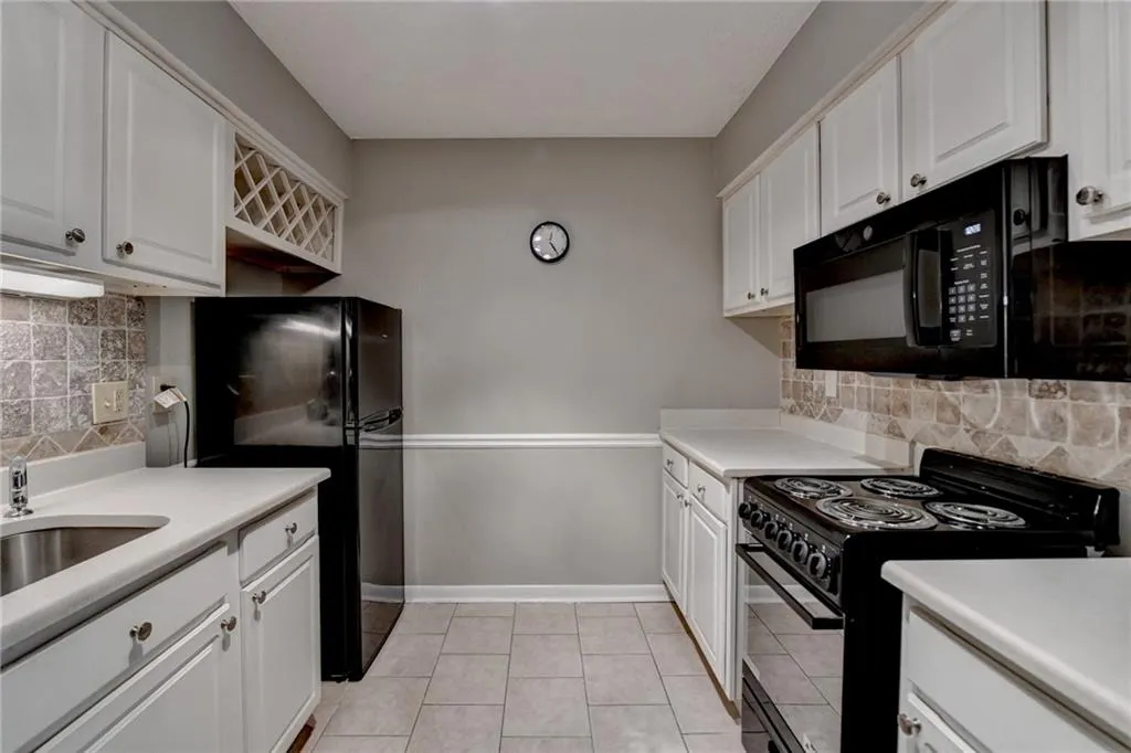 Kitchen featuring white cabinets, light tile patterned floors, baseboards, and black appliances