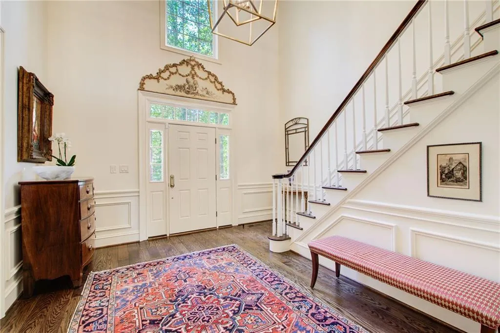 Entrance foyer with a wainscoted wall, a decorative wall, dark wood-style floors, a chandelier, and stairs Entrance foyer with a wainscoted wall, a decorative wall, dark wood-style floors, a chandelier, and stairs
