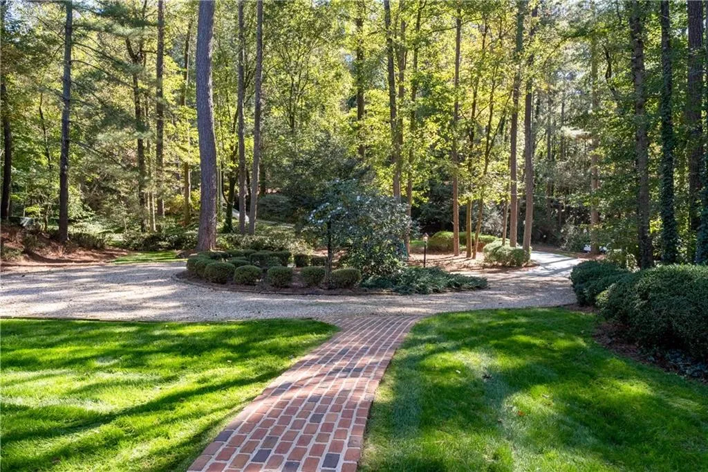 A gracious circular driveway framed by mature trees and lush landscaping offers an elegant first impression. The wide pea gravel drive provides easy access and ample guest parking while blending seamlessly with the natural surroundings. A charming brick walkway leads to the front entry, setting the tone for this serene and private setting just off the street.