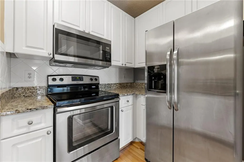 Kitchen featuring stainless steel appliances, white cabinetry, light stone countertops, and backsplash
