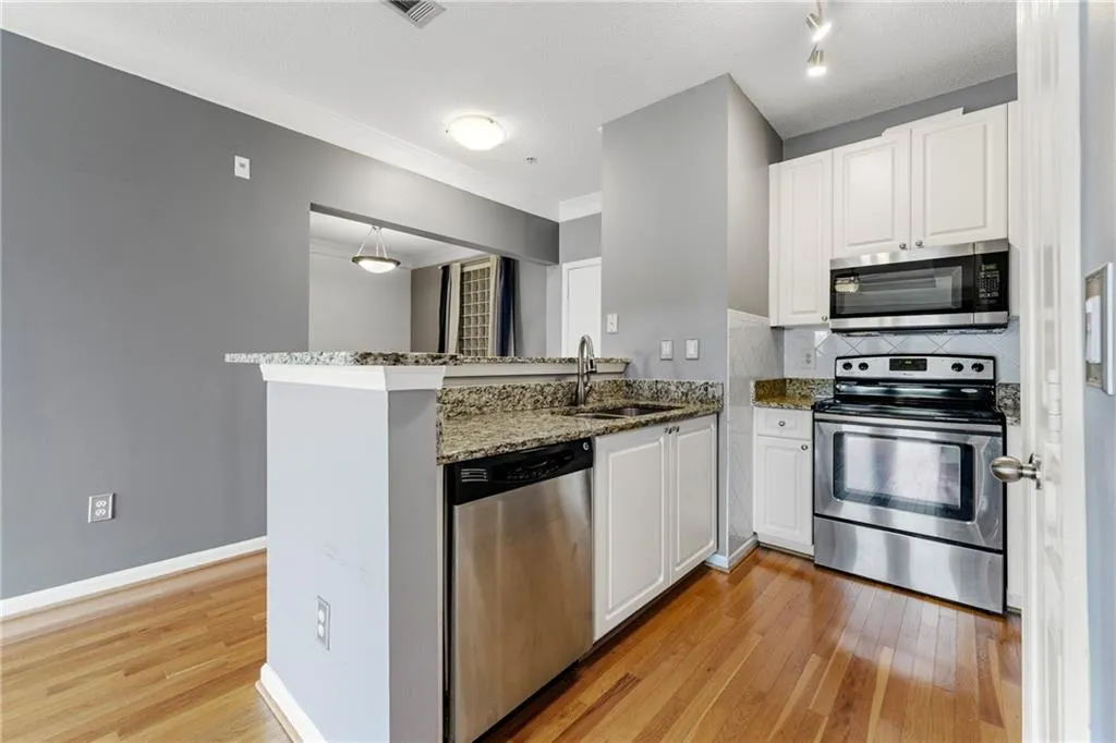 Kitchen featuring dark stone counters, appliances with stainless steel finishes, a peninsula, light wood-style flooring, and white cabinetry