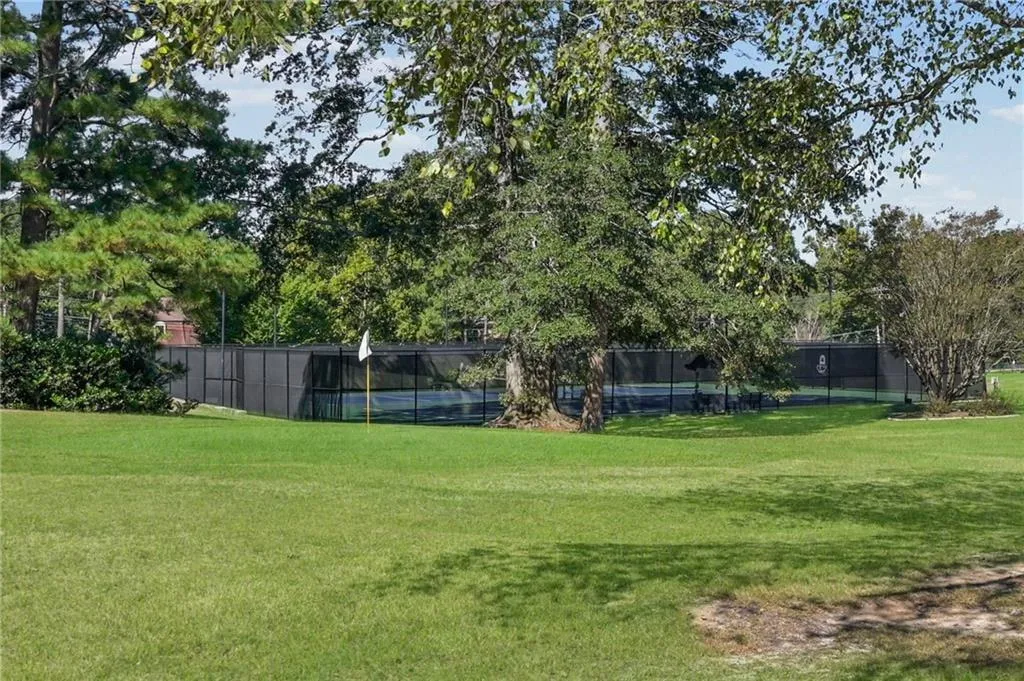 Expansive lawn featuring mature trees and a fenced tennis court and pickle ball courts