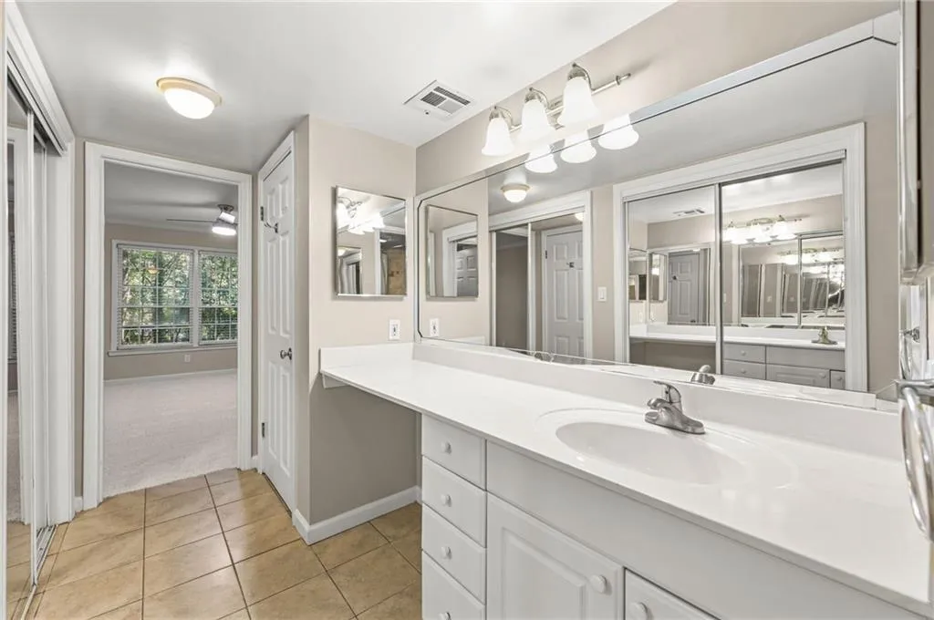 Extended vanity with integrated sink, tile flooring, wall-mounted mirror, and sliding mirrored closet doors