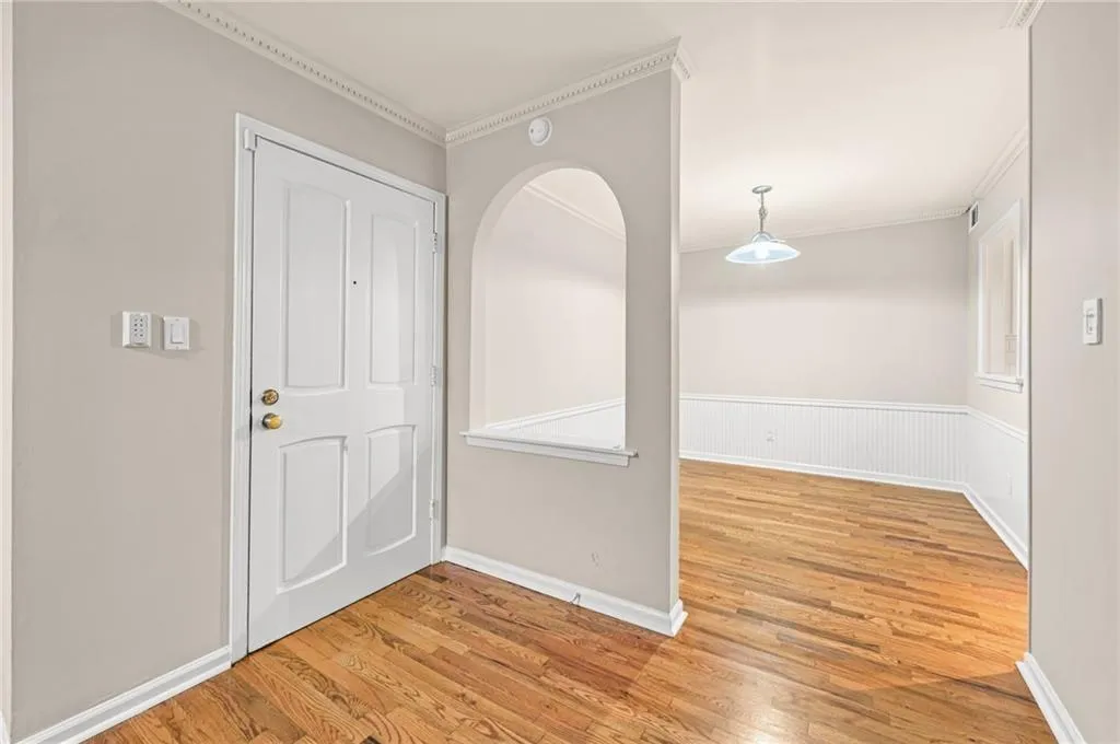 Hardwood flooring, crown molding, arched entry, beadboard wainscoting, and a ceiling-mounted light fixture