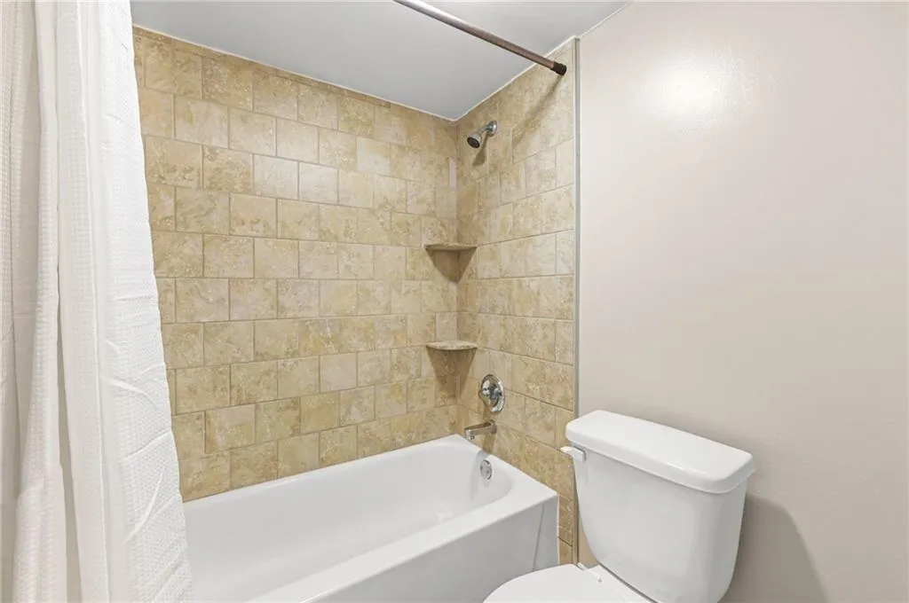 Tile-surround shower with built-in corner shelving, chrome fixtures, and white tub