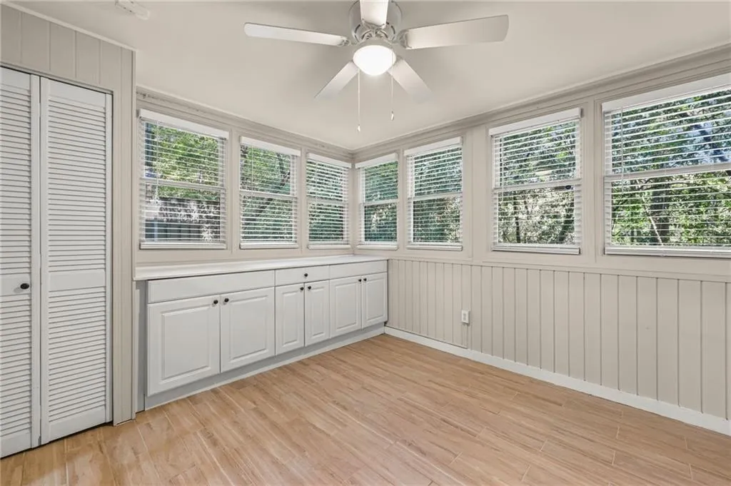 Wood-finish flooring with extensive multi-pane windows, a ceiling fan, and built-in white cabinetry with a light-toned countertop
