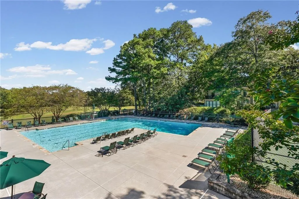 Expansive outdoor swimming pool with surrounding concrete decking, lounge seating, and adjacent tennis court